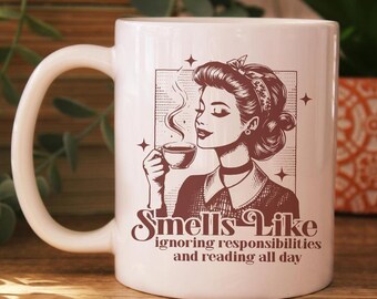 Könnte beinhalten: Weißer Keramikbecher mit einer Vintage-Illustration einer Frau, die Kaffee trinkt. Der Becher hat den Text "Smells Like ignoring responsibilities and reading all day" in brauner Schrift. Ein tolles Geschenk für Leser.