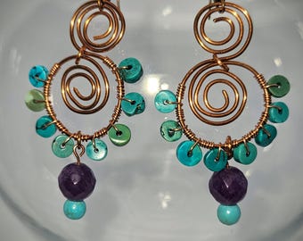 May include: A pair of dangle earrings featuring copper wire formed into two stacked spirals. The larger bottom spiral is adorned with small, round turquoise-colored beads along the outer edge, with a faceted purple bead and a turquoise bead at the base.