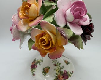 Peut inclure: Un arrangement floral en céramique avec un bouquet de roses oranges, roses et bordeaux. Les roses sont placées dans un vase blanc avec un motif floral. Une pièce décorative.