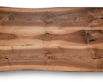 May include: A rectangular wooden table top with a natural edge. The wood grain is visible, with shades of brown and tan. The table top is approximately 60 inches long and 24 inches wide.