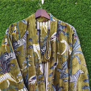 May include: Olive green velvet robe with a jungle animal print featuring zebras, leopards, and birds. The robe has a striped trim on the cuffs and a matching belt. The fabric has a soft, luxurious appearance.