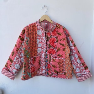 Puede incluir: Chaqueta acolchada en tonos rosa, naranja y blanco, adornada con estampados florales. La chaqueta presenta cuello mandarín, mangas largas y cierre de botones. La chaqueta mide aproximadamente 61 cm de largo.