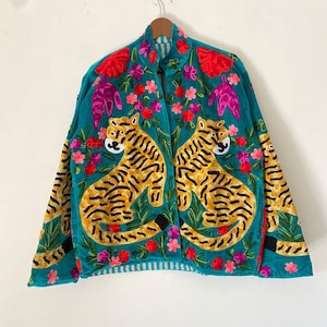 Peut inclure: Veste turquoise ornée de broderies de tigres et de motifs floraux. La veste présente deux tigres se faisant face, avec des rayures jaunes et noires. Des fleurs rouges, roses et violettes sont dispersées sur la veste, avec des motifs floraux sur les manches.