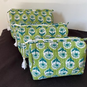 May include: Three green cosmetic bags with a floral pattern in teal and white. Each bag has a white zipper and a tassel. The bags are rectangular and appear to be made of quilted fabric.