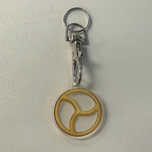 May include: A keyring with a silver clasp and ring. The charm is a clear circle with a yellow peace sign design. A simple accessory.