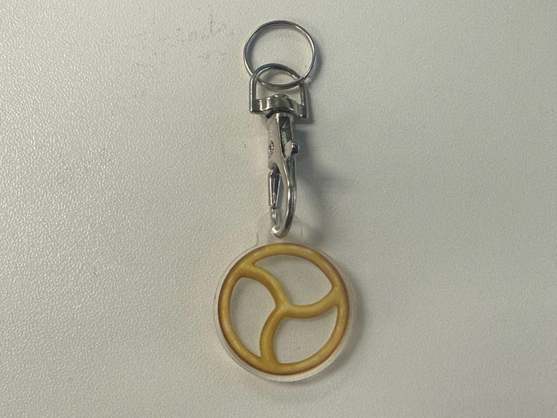 May include: A keyring with a silver clasp and ring. The charm is a clear circle with a yellow peace sign design. A simple accessory.