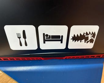 May include: Three white square stickers with black icons. The first shows a fork and knife, the second a person in bed, and the third a person running through trees. The stickers are on a black surface with a red and black edge.