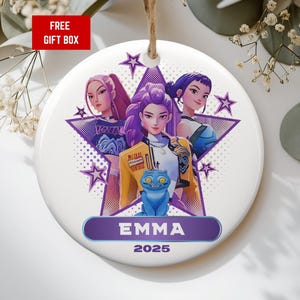 May include: White ceramic ornament with a cartoon illustration of three women in front of a purple star. The ornament has the name "EMMA" and the year "2025" printed on it. A red box with the text "FREE GIFT BOX" is visible.