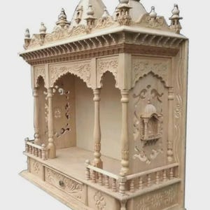 Puede incluir: Un templo o santuario de madera tallada de color claro y con intrincados detalles. La estructura presenta m&uacute;ltiples niveles, aberturas arqueadas y tallas en relieve detalladas. Tiene un peque&ntilde;o caj&oacute;n y una barandilla decorativa. El dise&ntilde;o es sim&eacute;trico y ornamentado.