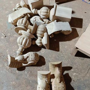 Puede incluir: Una colecci&oacute;n de tallas de madera sin terminar, de color claro, que incluyen pin&aacute;culos, elementos decorativos y detalles arquitect&oacute;nicos. Las piezas var&iacute;an en tama&ntilde;o y forma, algunas con dise&ntilde;os tallados intrincados. Los objetos est&aacute;n esparcidos sobre una superficie de hormig&oacute;n.