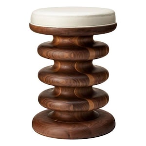 May include: A stool featuring a smooth, off-white circular seat cushion atop a dark brown wooden base. The base is constructed with four stacked, rounded, ring-like segments that taper and widen, creating a distinct, symmetrical, ribbed profile.