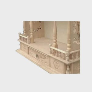 Puede incluir: Un templo de madera de color claro con intrincadas tallas. El dise&ntilde;o incluye un caj&oacute;n con pomo, patrones florales decorativos y barandillas de balaustrada. La estructura presenta pilares y una estanter&iacute;a, mostrando una artesan&iacute;a detallada.