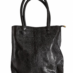 May include: Black tote bag with a snakeskin texture. The bag features two braided handles and a zip closure. The bag is made from a textured material and has a rectangular shape.