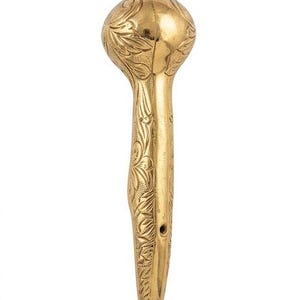 Könnte beinhalten: Ein polierter goldfarbener Metallgriff mit einem verzierten, gravierten Blumenmuster auf der abgerundeten Oberseite und dem sich verjüngenden Körper. Das Objekt hat eine glatte, reflektierende Oberfläche mit sichtbaren Ätzungen und zwei kleinen runden Löchern nahe der Basis.