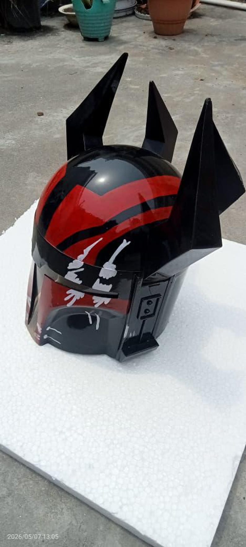 Puede incluir: Un casco negro y rojo con detalles angulares y puntiagudos. El casco presenta un acabado brillante con rayas rojas y detalles gr&aacute;ficos blancos. El dise&ntilde;o sugiere un tema futurista o de ciencia ficci&oacute;n.