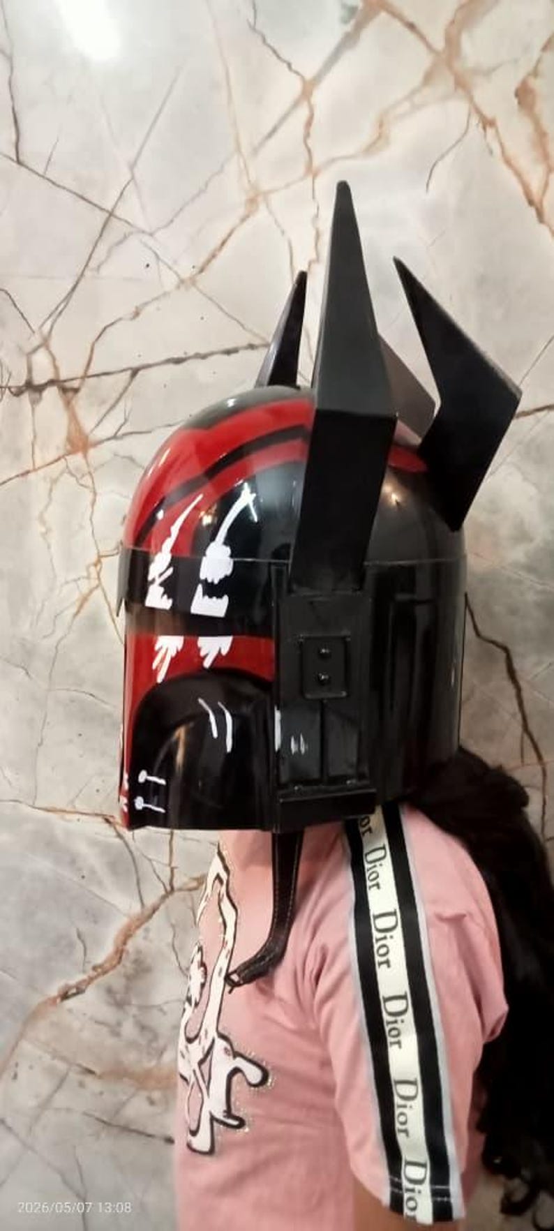 Puede incluir: Un casco negro y rojo con un dise&ntilde;o &uacute;nico, con formas angulares y un acabado brillante. El casco tiene acentos negros prominentes y una franja roja. El dise&ntilde;o incluye detalles gr&aacute;ficos blancos.