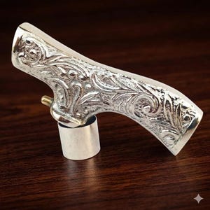 Könnte beinhalten: Ein silberner Flaschenverschluss mit einem verzierten, gravierten Blumendesign. Der Verschluss hat einen gebogenen Griff und einen zylindrischen Sockel. Das Metall hat eine polierte Oberfläche, und das Design ist detailliert mit Blättern und Wirbeln.