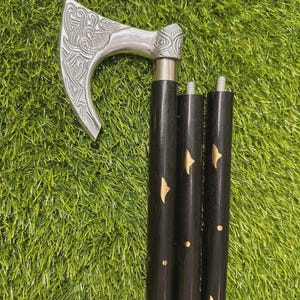 以下が含まれることがあります： 銀色の斧頭の杖。装飾的なハンドルと黒い木製のシャフトが付いています。斧頭には複雑な彫刻模様があります。シャフトは3つのセクションで構成され、金色の星型のアクセントが付いています。