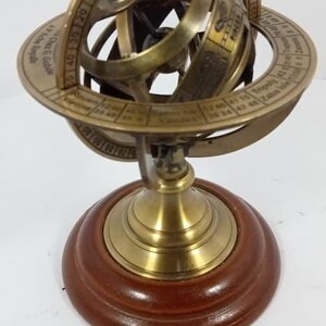 Könnte beinhalten: Eine Armillarsphäre aus Messing mit Holzsockel. Die Sphäre hat mehrere Ringe mit Gradmarkierungen und Tierkreiszeichen. Der Sockel ist dunkelbraun. Ein dekorativer Himmelsglobus.