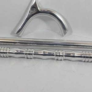 May include: Silver-colored walking cane components, including a curved handle, a long shaft, and a decorative lower section. The cane's parts are laid out against a white background, showcasing the metallic finish and design details.