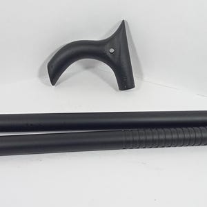 May include: A black, disassembled walking cane with a curved handle. The cane is in three parts: the handle, a smooth cylindrical section, and a textured cylindrical section. The cane is designed to be assembled.