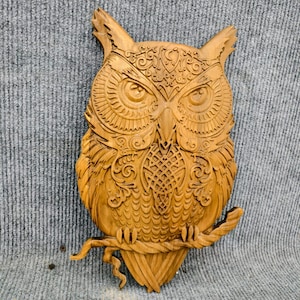 May include: A detailed wooden owl carving, with intricate patterns and textures. The owl is perched on a branch, with its wings and feathers meticulously carved. The artwork is a warm, natural wood tone, suitable for home decor.