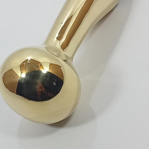 May include: A gold-colored, elongated object with a rounded end and a smooth, reflective surface. The object has a bulbous shape at one end and tapers to a narrower form. It appears to be made of metal.