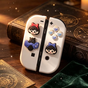May include: A pair of white game controller attachments featuring decorative silicone charms. The left side displays a character with a red bow and a black cat with a blue bow. The right side features four small potion bottle charms and a character with a blue bow.
