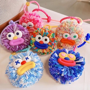 May include: A selection of vibrant, fluffy hair ties, each adorned with a cartoon face. The ties showcase a spectrum of colours, such as pink, purple, blue, and rainbow, with oversized eyes, noses, and mouths. Every tie has a unique expression, adding a playful element to the accessories.