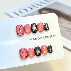 Peut inclure: Un ensemble de dix faux ongles présentés sur une carte blanche avec l'inscription HANDMADE Nail. Les ongles présentent un mélange de finitions brillantes roses et noires, décorés de motifs léopard, de petites étoiles argentées et de points.