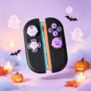 May include: A pair of black gaming controllers featuring custom silicone thumbstick caps. The left controller has a white ghost-shaped d-pad cover and a purple-topped cap. The right controller has purple button covers and a purple ghost cap.