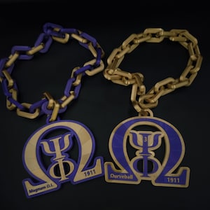 May include: Two decorative chain necklaces with pendants. One necklace has a gold chain with a purple chain link, and the other has a gold chain. Each pendant features a purple and gold design with the year 1911 and text.