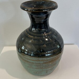 May include: A handcrafted ceramic vase with a dark blue and teal glaze. The vase has a rounded body and a flared rim. The lower portion of the vase is teal, transitioning to dark blue at the top. A decorative piece for the home.