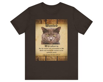 Puede incluir: Camiseta marrón oscuro con un diseño de cartel de "Se busca". El cartel presenta un gato gris y la palabra "Whiskers", junto con texto que detalla los presuntos crímenes del gato. Una prenda de vestir casual y humorística.