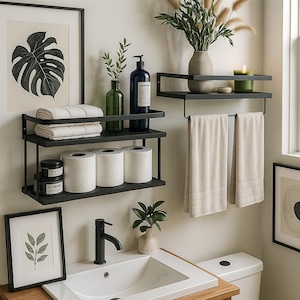 May include: A modern bathroom scene featuring black metal shelves holding white towels, toilet paper, and decorative jars. A white sink with a black faucet sits on a wooden vanity. Framed art and plants add to the decor.