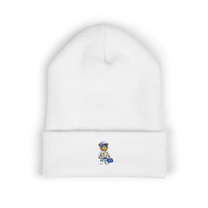 May include: White beanie hat featuring an embroidered bear wearing sunglasses, a patterned outfit, and a blue bag. The hat is made of a soft, knitted material.