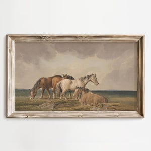 Puede incluir: Una impresión vintage enmarcada representa una manada de caballos en un campo bajo un cielo nublado. Los caballos son de varios colores, incluyendo marrón, blanco y beige. La obra de arte está enmarcada en un marco de madera marrón claro desgastado.