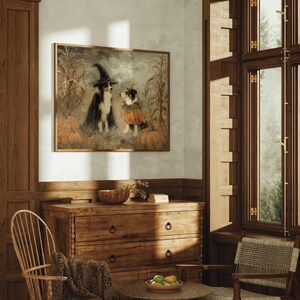 May include: A framed wall art print depicting two dogs in a field with pumpkins. One dog wears a black witch hat and cape, while the other wears a pumpkin-shaped collar. The scene features tall corn stalks and a muted, earthy color palette.