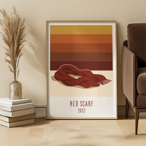 May include: A framed art print with a red scarf illustration. The artwork has a minimalist design with a gradient background of orange and brown hues. The text "RED SCARF 2012" is printed at the bottom.