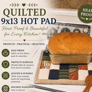 May include: A square quilted hot pad featuring a patchwork design of cream, navy blue, and olive green fabric squares with paisley and striped patterns. A glass loaf pan containing a loaf of bread sits on the pad next to a wooden utensil.
