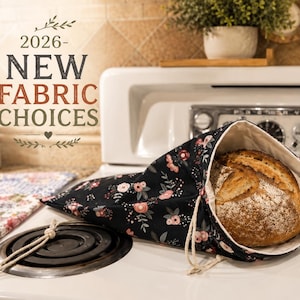 May include: A round loaf of bread inside a black bread bag with a floral pattern. The bag is open, revealing the bread. The text "2026 - NEW FABRIC CHOICES" is at the top of the image.