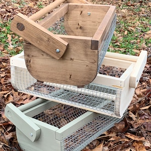 May include: Two wooden baskets with wire mesh bottoms. The top basket is stained brown and the bottom basket is painted light green. Both baskets have wooden handles.