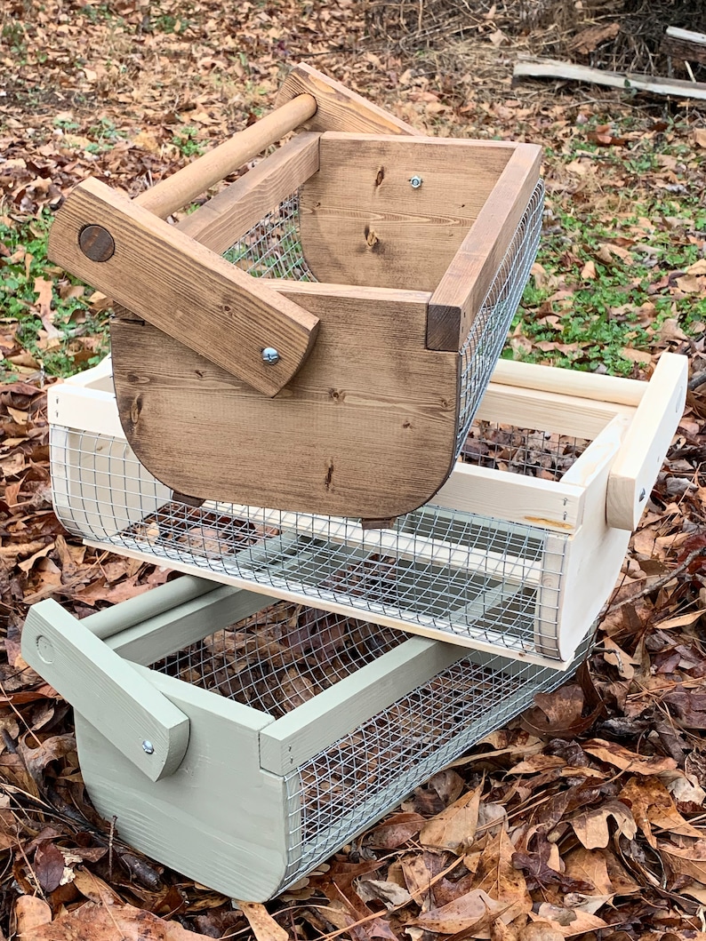 May include: Two wooden baskets with wire mesh bottoms. The top basket is stained brown and the bottom basket is painted light green. Both baskets have wooden handles.