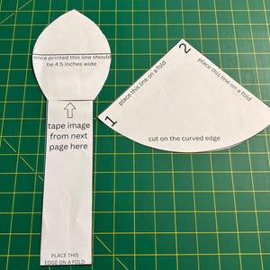 May include: Two white paper sewing patterns with black text. The left piece is a long shape with a pointed top, labeled 'once printed this line should be 4.5 inches wide'. The right piece is a fan shape labeled 'place this line on a fold'.