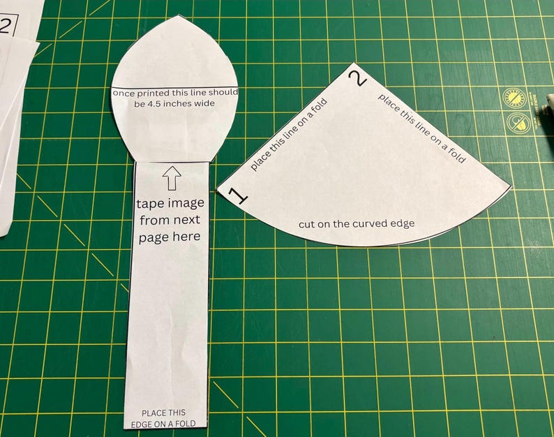May include: Two white paper sewing patterns with black text. The left piece is a long shape with a pointed top, labeled 'once printed this line should be 4.5 inches wide'. The right piece is a fan shape labeled 'place this line on a fold'.
