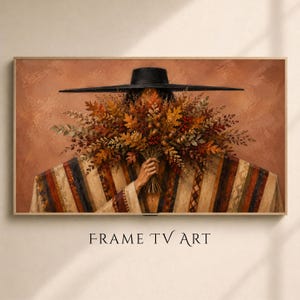 May include: A rectangular digital print titled FRAME TV ART featuring a person wearing a wide-brimmed black hat and a striped poncho, holding a large bouquet of autumn leaves, berries, and dried foliage against a solid terracotta background.