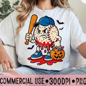 Puede incluir: Camiseta gris claro con un personaje de béisbol de dibujos animados que sostiene un bate. El béisbol tiene una expresión enfadada, chispas de colores, una gorra azul y zapatos azules. Una cesta de calabaza y murciélagos completan el tema de Halloween.