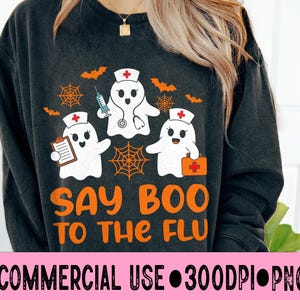 May include: Dark gray sweatshirt with a Halloween-themed design. The design features three white ghost characters dressed as nurses, orange bats, spiderwebs, and the text "SAY BOO TO THE FLU" in orange. The sweatshirt is a comfortable, casual style.