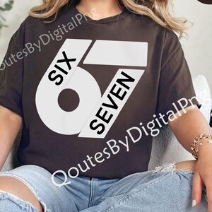 May include: A brown t-shirt with the text "SIX 6 SEVEN" in a bold, white font. The shirt is a casual style, with a round neckline and short sleeves. The design is centered on the front of the shirt.