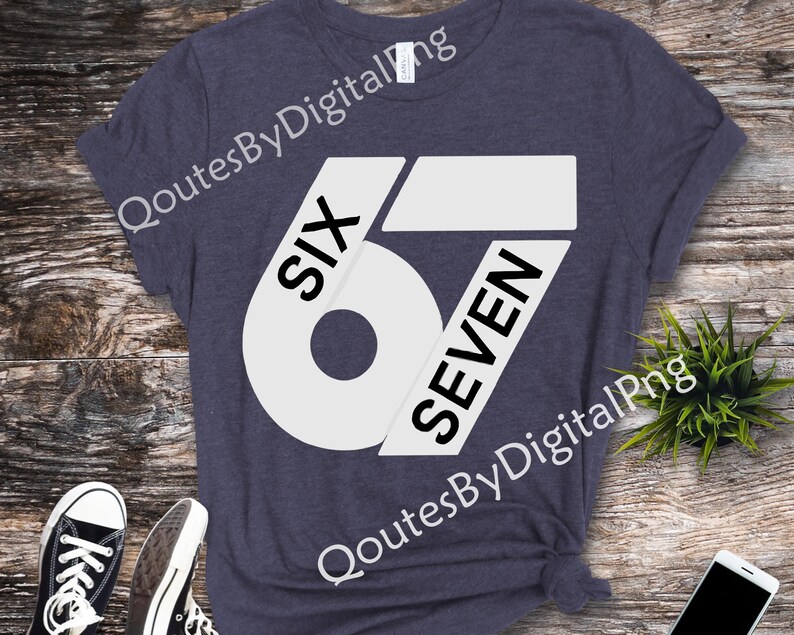 May include: A navy blue t-shirt with a large white graphic design featuring the numbers "67" and the words "SIX" and "SEVEN". The shirt is displayed on a wooden surface with sneakers and a phone.